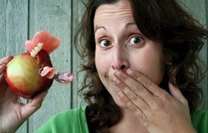 Woman holding an apple with dentures stuck in it